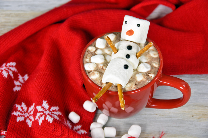 Hot chocolate drink and marshmallow snowman in red mug with red winter scarf.