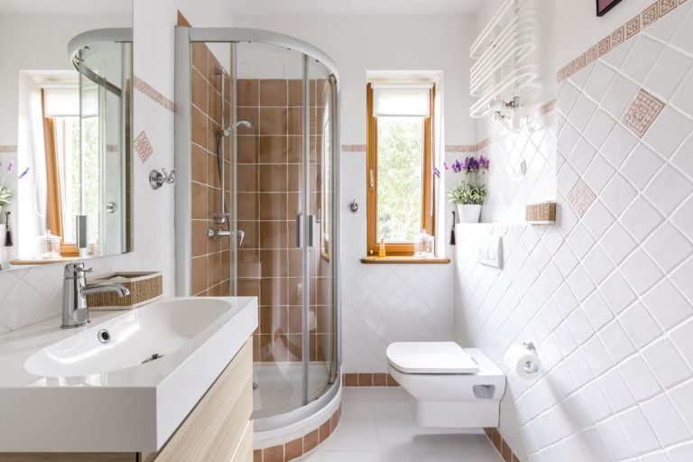 Glass shower in small white bathroom with sink, mirror and toilet