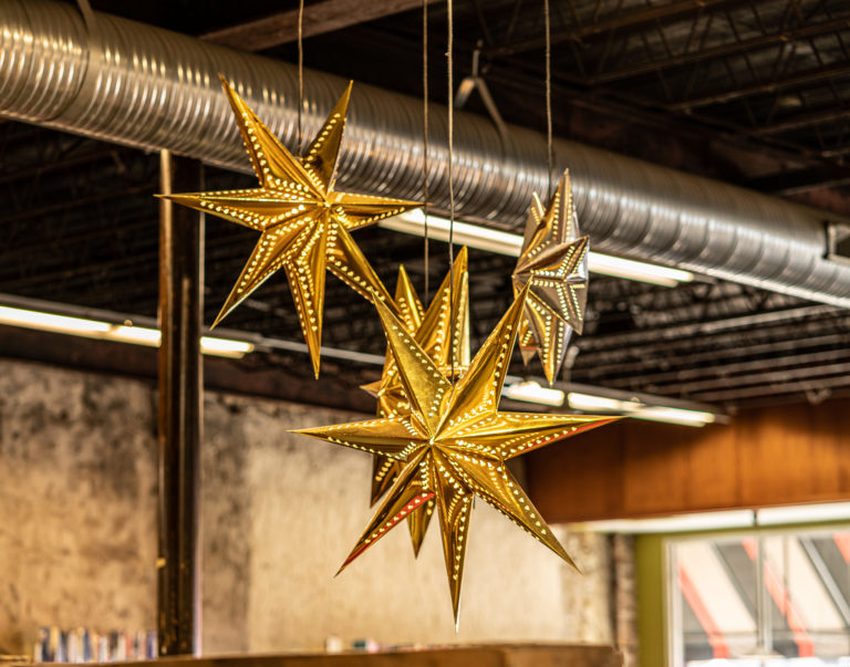 A gold star-shaped lantern made out of paper hanging from a ceiling. There are lights inside it which are projecting star shapes all around. Decorative golden glowing stars hanging in a loft.
Beloit, Rock County, Wisconsin, USA